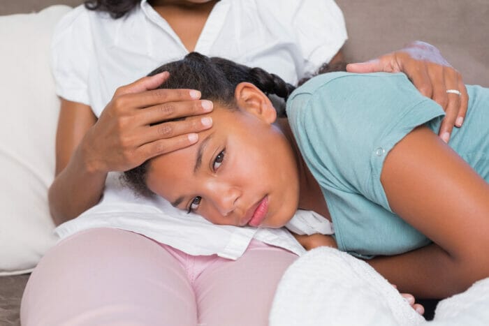 Sick daughter lying on mothers lap at home in living room